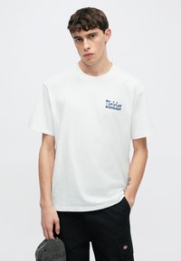 Λευκό βαμβακερό T-shirt με το μπλε κεντημένο λογότυπο "Dickies" στο αριστερό στήθος, σε συνδυασμό με μαύρο cargo παντελόνι.