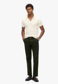 Hvid strikket polo-shirt med korte ærmer, kombineret med mørkegrønne bukser og brune loafers. Har krave med en knap.