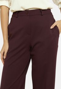 Vīna krāsas bikses ar gludu tekstūru, vienu pogas aizdari, sānu kabatām un pieguļošu griezumu.