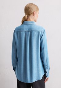 Jasnoniebieska koszula denims z karczkiem, z guzikami przy mankietach i luźnym krojem. Charakteryzuje się klasycznym kołnierzykiem i gładką fakturą.