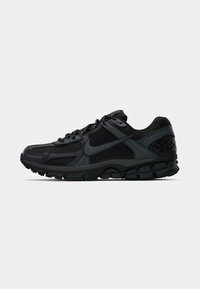 Scarpa sportiva nera con una tomaia in rete e sintetico, caratterizzata da una suola testurizzata, lacci e un tallone sagomato per supporto.