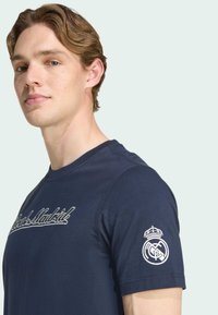Camiseta de algodón azul marino con bordado de 'Real Madrid' en el pecho y el logo del club en la manga izquierda. Mangas cortas, escote redondo.