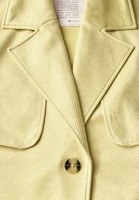 Blazer con motivo a spina di pesce in morbido tessuto giallo chiaro, con rever a punta, caratterizzato da un bottone tondo e trasparente e dettagli di cucitura.