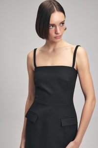 Schwarzes, tailliertes Kleid mit quadratischer Ausschnitt, dünnen Trägern und zwei kleinen aufgesetzten Taschen an der Taille. Glattes Material mit minimaler Textur.