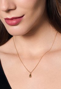 Złoty naszyjnik z wisiorkiem w kształcie kropli, zawieszony na delikatnym dopasowanym łańcuszku. Gładka powierzchnia z odbijającym się wykończeniem.
