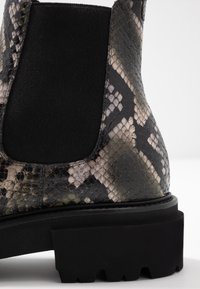 Botín de tobillo con estampado de serpiente en negro y gris, con paneles laterales elásticos, parte superior de cuero texturizado y suela gruesa negra con surcos de tracción.