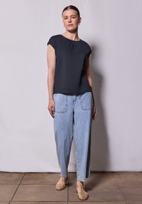 Top de marina de manga corta, corte relaxed, combinado con unos vaqueros de cintura alta de color azul claro que tienen dos grandes bolsillos frontales y unas sandalias de yute beige.