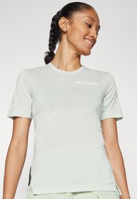 Šviesiai žalia Terrex trumpą rankovę marškiniai su apvalia iškirpte, tinklinėmis detalėmis ant rankovių ir šonų, su balta logo ant krūtinės. Minkšta tekstūra.