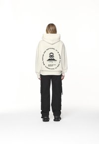 Vit huvtröja med grafiskt tryck på baksidan, kombinerad med svarta cargo-byxor. Anmärkningsvärda egenskaper: oversized passform, mjukt tyg.