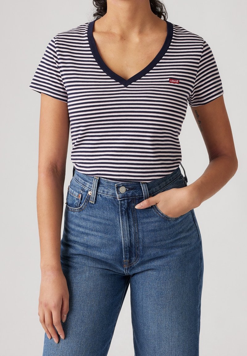 Camiseta de algodón a rayas con un escote en V azul marino y mangas cortas, con un pequeño logo de Levi's en el pecho, combinada con unos pantalones vaqueros de cintura alta azules.