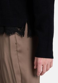 Czarny dzianinowy sweter z koronkową lamówką na dolnym brzegu, o prążkowanej fakturze i długich rękawach, zestawiony z beżowymi spodniami z satyny.