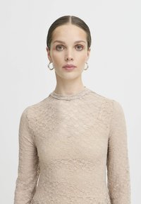 Spitzenoberteil in hellem Beige mit dezentem Blumenmuster, hohem Halsauschnitt und langen Ärmeln. Glatte Textur mit taillierter Silhouette.