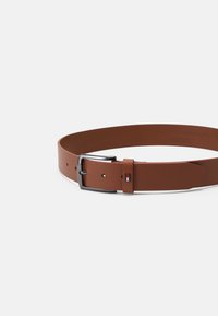 Cintura in pelle marrone con una superficie liscia, dotata di una fibbia in metallo argentato e di un piccolo accento rettangolare del marchio in rosso e blu.