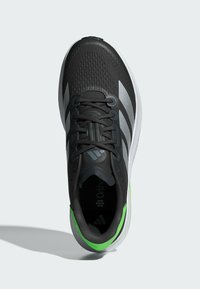 Čierne športové topánky s vrchnou časťou z mriežky, striebornými akcentmi a zeleným detailom na päte. Obsahujú šnurovanie a dizajn s polstrovanou podrážkou.