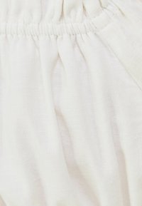 Biała, teksturowana tkanina z elastycznym detalem w talii, tworzącym miękkie fałdy i lekki wygląd.