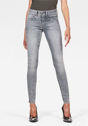 Jeans ajustados grises de mezclilla, con una cintura alta, diseño de cinco bolsillos y un ligero desgastado. Se combinan con zapatos de tacón negros.