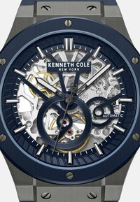 Zegarek Kenneth Cole ma granatową tarczę z wzorem skeleton, srebrne akcenty, automatyczny mechanizm oraz stalową kopertę.