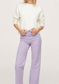 Pull blanc à manches longues, associé à un pantalon lavande taille haute, avec une coupe droite et des poches latérales.