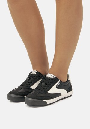 Zapatillas en blanco y negro con material de ante y malla, que presentan un diseño con cordones, suela de goma y detalle del logo en la lengüeta.