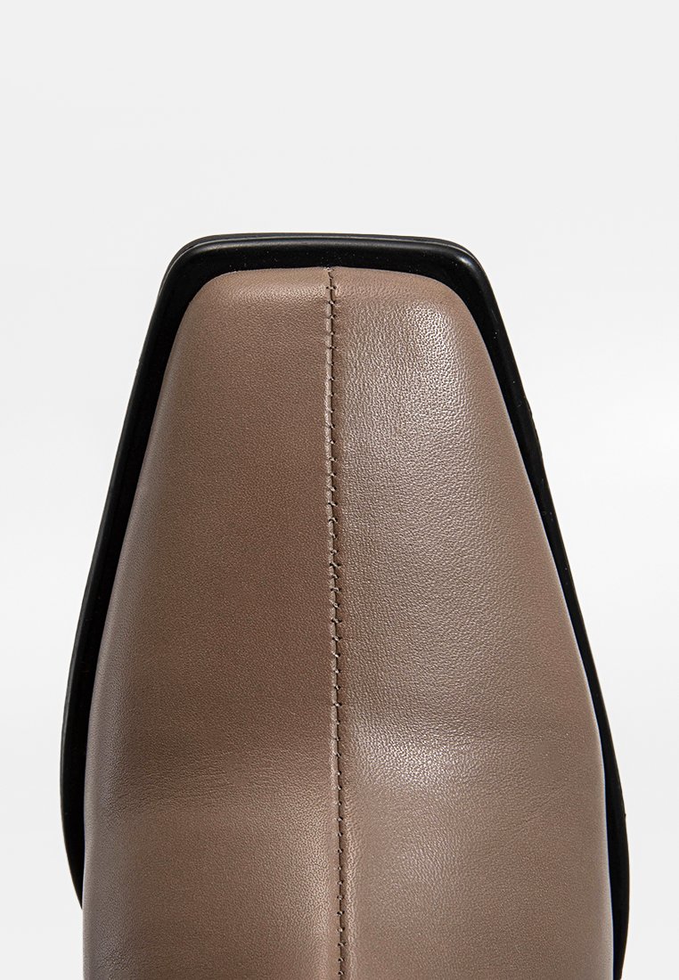 Bruine lederen schoen met een vierkante neus, voorzien van een zwarte accent langs de rand en zichtbare stiksels in het midden.