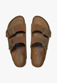 Bruine suède sandalen met twee verstelbare bandjes en zilveren gespen. Orthopedische voetbed met blauwe merklettering, maat 38 is aan de binnenkant gedrukt.