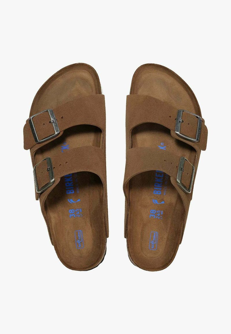 Bruine suède sandalen met twee verstelbare bandjes en zilveren gespen. Orthopedische voetbed met blauwe merklettering, maat 38 is aan de binnenkant gedrukt.