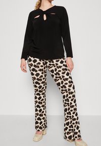 Maglietta nera a maniche lunghe con un dettaglio ritagliato attorcigliato sullo scollo, abbinata a pantaloni a zampa d'elefante con stampa leopardo. L'outfit è completato da tacchi a blocco beige.