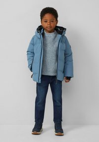 Veste rembourrée légère bleue avec capuche, doublure noire et fermeture éclair ; associée à un pull texturé bleu clair et un jean en denim foncé. Baskets à semelle beige.