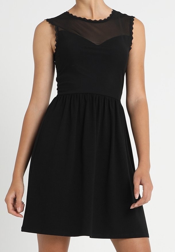 Robe noire sans manches avec empiècement en mesh transparent, encolure festonnée, taille cintrée et jupe froncée longueur genou portée par une femme.
