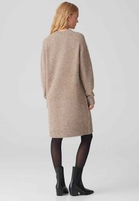 Abito maglione a maglia metallica beige con maniche lunghe, vestibilità rilassata e polsini a coste, abbinato a stivaletti neri alla caviglia e collant opachi.