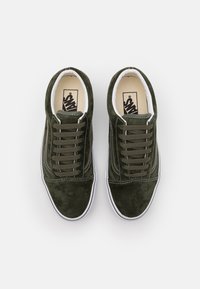 Olivově zelené semišové tenisky s bílou podešví, odpovídajícími tkaničkami a kontrastním bílým prošíváním. Klasický nízký design s béžovou vnitřní podšívkou.