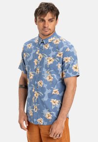 Kortebloezemknopshirt in een blauw camouflagepatroon met bloemaccenten in perzik en geel. Beschikt over een borstzak en een subtiele glans.