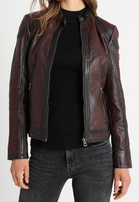 Burgunderrote Leder-Motorradjacke mit tailliertem Design, Reißverschluss vorne, Schulterdetails und seitlichen Taschen. Kombiniert mit einem schwarzen Oberteil.
