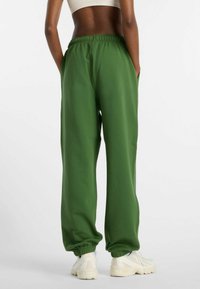 Grüne Jogginghose mit elastischem Bund, Seitentaschen und gerippten Bündchen an den Knöcheln. Hergestellt aus einem weichen, glatten Stoff.