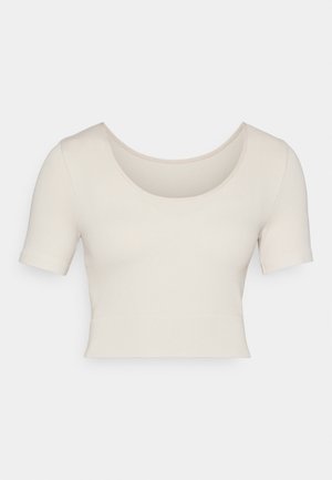 Īsām piedurknēm, apgriezts tops vieglā bēšā ribota auduma. Tam ir plaša apaļā izgriezuma kakla līnija un pieguloša piegriezuma forma, izceļot gludu tekstūru.