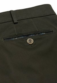 Poche arrière de pantalon en tissu texturé vert foncé avec une fermeture à bouton gravée "MEYER" et une boucle de ceinture visible au-dessus.