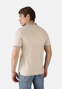 Polo shirt beige a maniche corte con colletto e polsini a coste, caratterizzato da una superficie liscia e uno spacco laterale all'orlo, abbinato a jeans blu chiaro.
