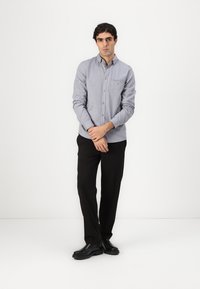 Lichtblauw overhemd met lange mouwen en zak, gecombineerd met zwarte broek en zwarte schoenen. Glad stof, net ontwerp.