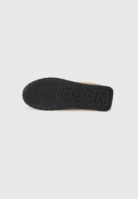 Black rubber outsole with textured grip patterns and bold “HUGO” branding, complementing a tan upper design.