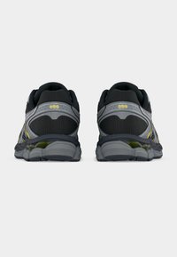 Μαύρα και γκρι παπούτσια τρεξίματος με υφασμάτινη επάνω επιφάνεια με υφή, μαξιλαρωμένη φτέρνα, αντανακλαστικές λεπτομέρειες και κίτρινα στοιχεία στο πίσω μέρος.