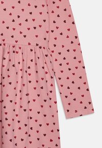 Abito rosa con un tessuto a trama che presenta piccoli cuori in diverse tonalità di rosso e rosso scuro, arricciato in vita e con maniche lunghe.