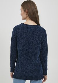 Pulover bleu marin cu un design tricotat texturat, manșete ondulate și un spate ușor alungit. Decolteu simplu de tip rotund, material moale.
