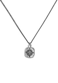Silverkompass-pendant på en tvinnad kedja. Pendeln har en texturerad yta och graverade kardinalriktningar, formad som en sten.