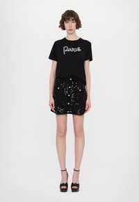 Schwarzes T-Shirt mit "Paris" aus Strass, kombiniert mit einem schwarzen Paillettenrock. Akzentuiert mit High-Heels. Schlichtes, tailliertes Design.