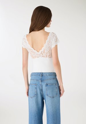 Body bianco con schiena in pizzo, scollatura a V profonda e maniche corte, abbinato a jeans a gamba larga a vita alta di colore azzurro chiaro.