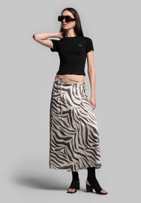 Black fitted T-shirt paired with a long, cream skirt featuring a black zebra print, cinched at the waist with a tie. Black heeled sandals.