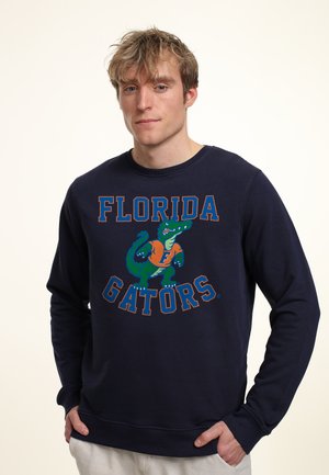 Marineblaues Sweatshirt mit dem Schriftzug "FLORIDA GATORS" und einem grünen Alligator-Graphic. Weicher Stoff mit gerippten Bündchen und Saum.