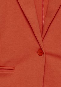 Oranžový blejzer s hladkým, štruktúrovaným materiálom. Výrazné detaily zahŕňajú zapínanie na jeden gombík a klopový golier.
