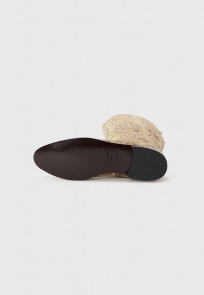 Botină tricotată cu un model animalier bej și maro, vârf rotund și talpă neagră pentru aderență. Design plat și suprafață superioară texturată.