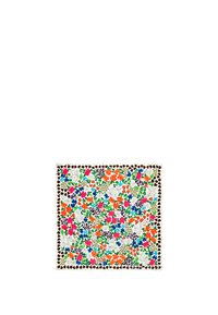 Bufanda de estampado floral que presenta colores vibrantes como rosa, azul, naranja y verde sobre un fondo blanco, terminada con un borde decorativo.